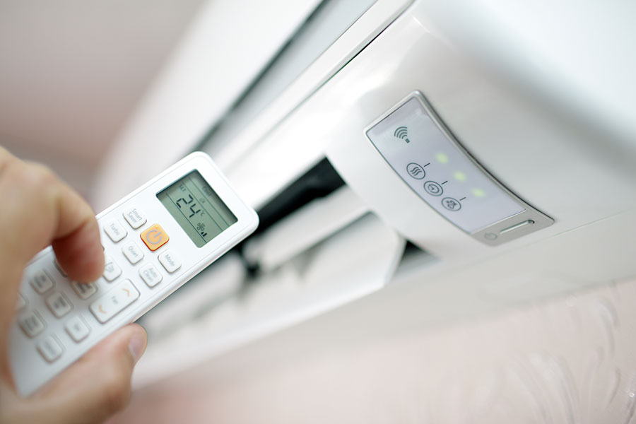 Hand Holding Air Conditioning Remote in Front of Air Conditioner | Air Conditioning Repairs, Air Conditioning Replacements & Installation for Smithtown, New York, and the Surrounding Areas